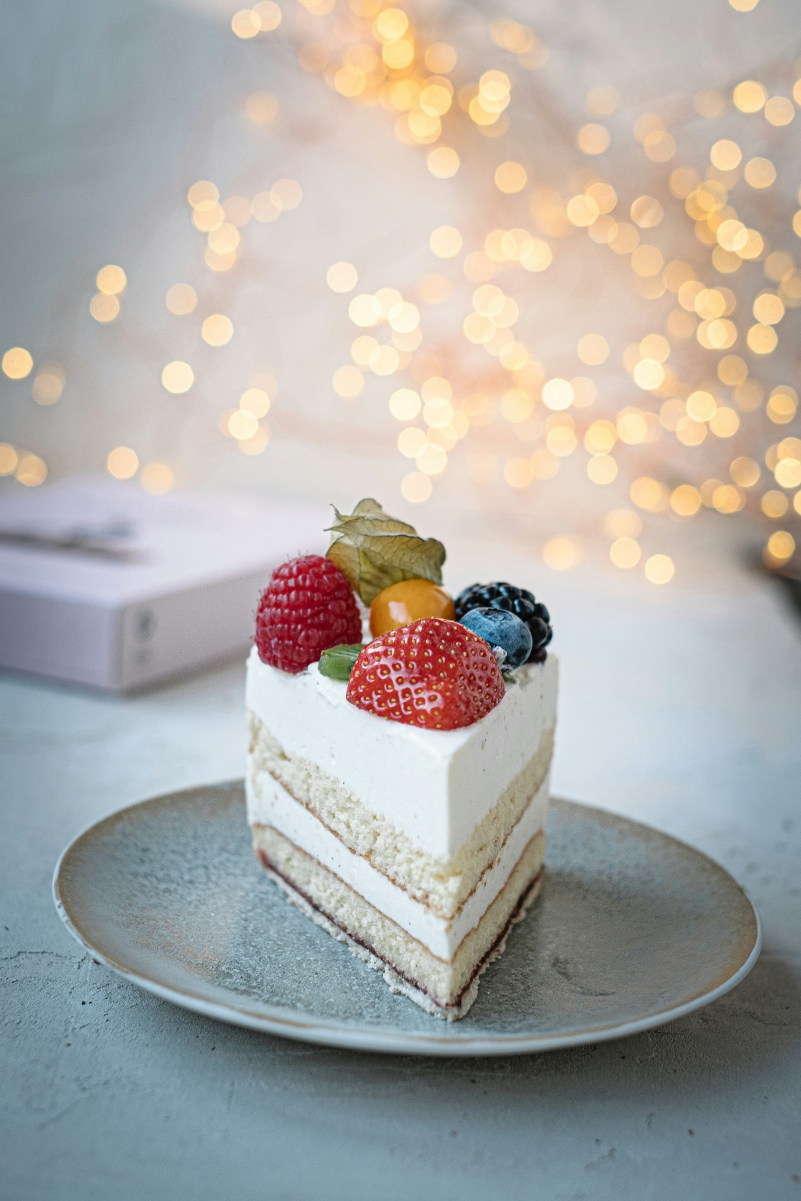 Rebanada de pastel de capas con crema y fresas frescas, con luces cálidas desenfocadas al fondo. Imagen representativa.