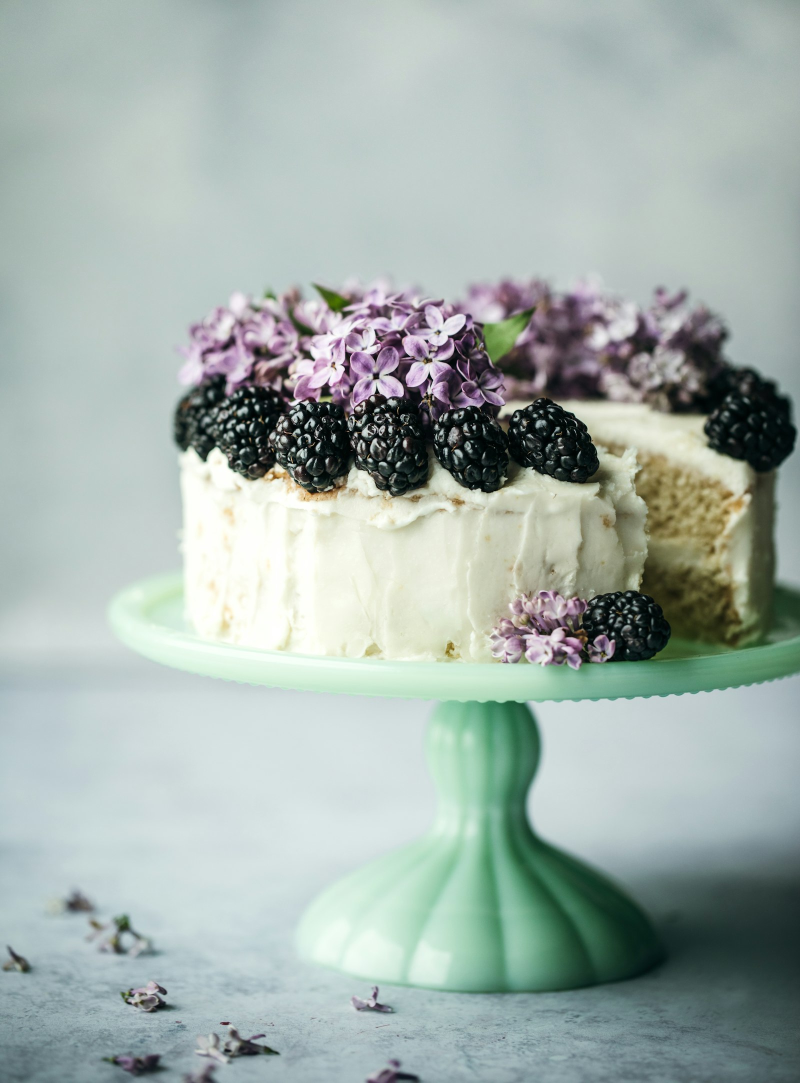 Pastel blanco decorado con zarzamoras y flores lilas sobre una base de cerámica verde jade. Imagen representativa, no es un pastel de La Roca.